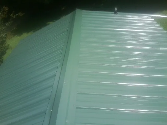 New green metal panels meeting at the ridge of a roof — Flat Roof Repair work by our crew in Newfane