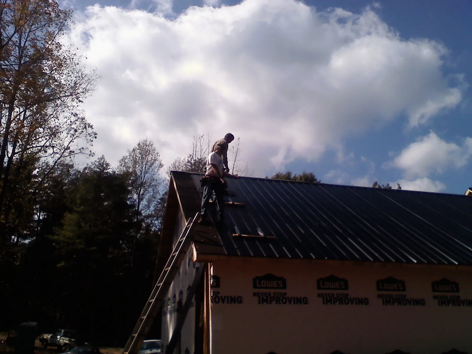 Roofer fastening dark metal panels high against a cloudy sky, from a Roof Inspection job in Newfane